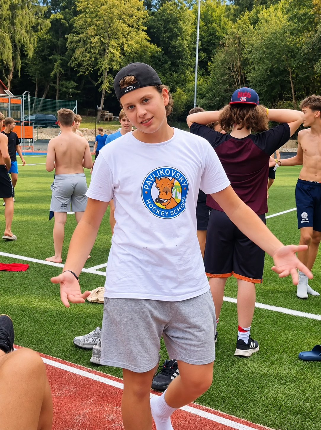 A young person wearing a hockey camp shirt with a group on an outdoor sports court.