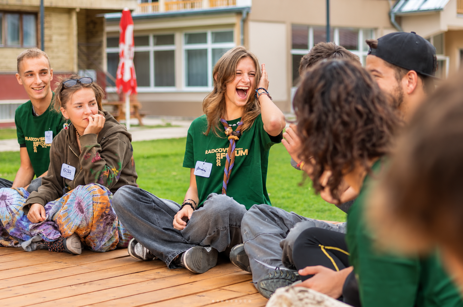 Young people sitting together on a wooden deck, talking and laughing.