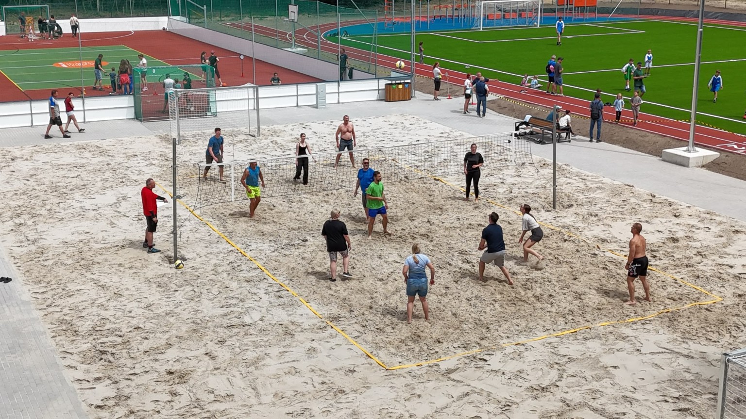 Guests playing beach volleyball with the sports grounds behind them