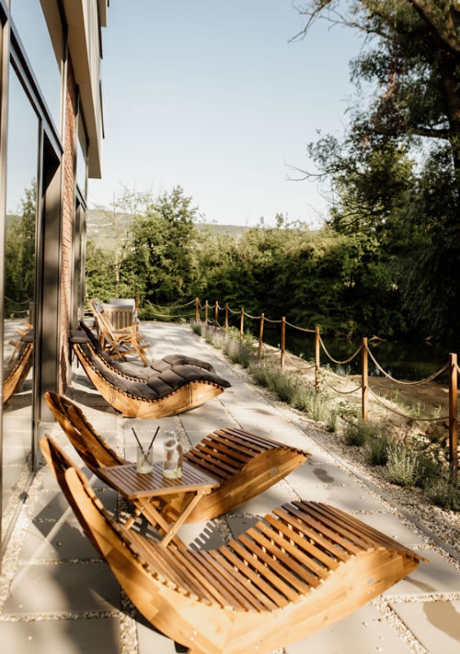 Outdoor relaxation area with wooden loungers beside trees and greenery.