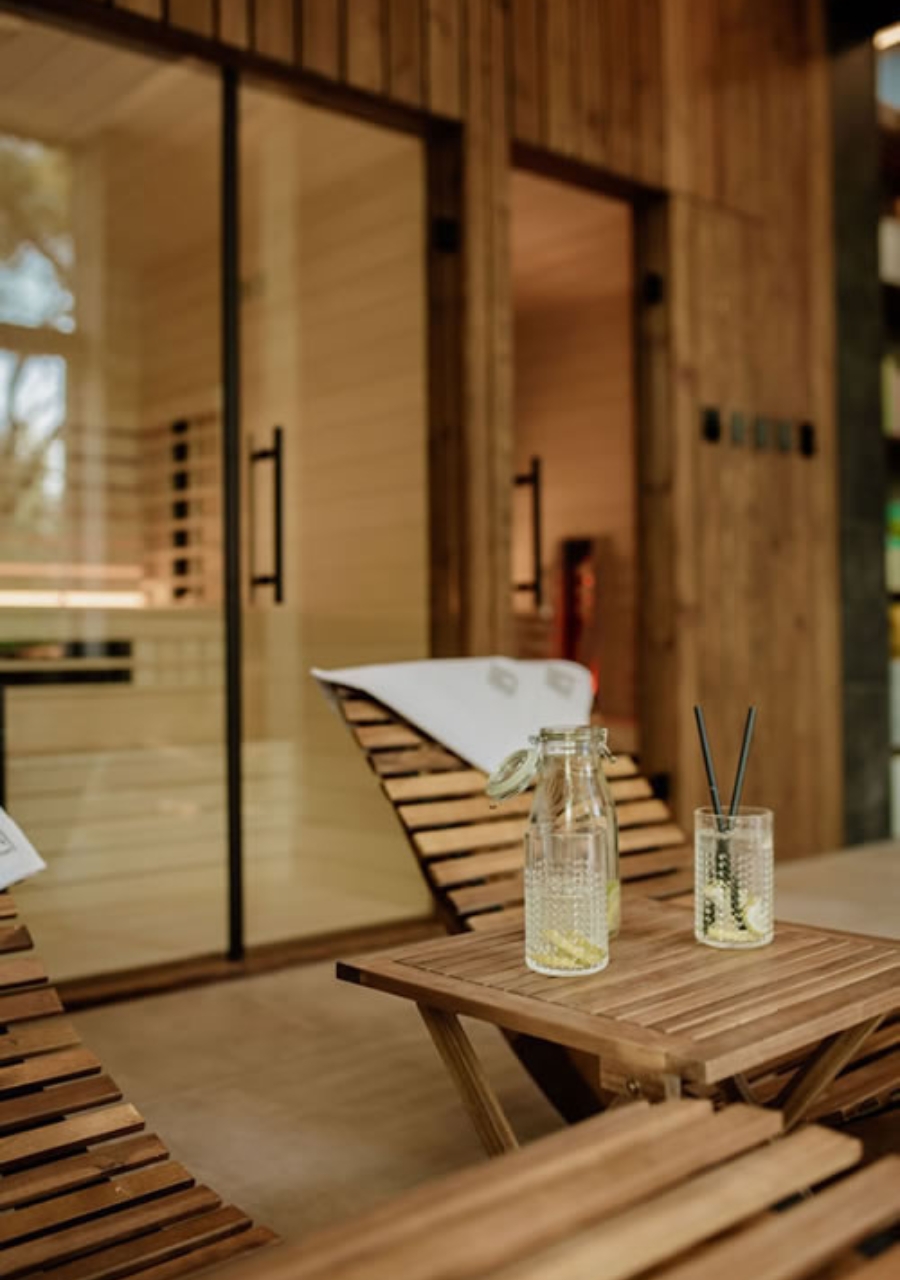 Wooden loungers and a table with drinks beside glass sauna doors.